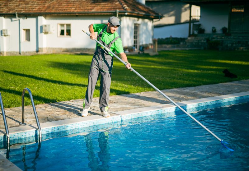 A Man cleaning pool with skimmer in Jacksonville, FL, as part of shock treatment & maintenance.
